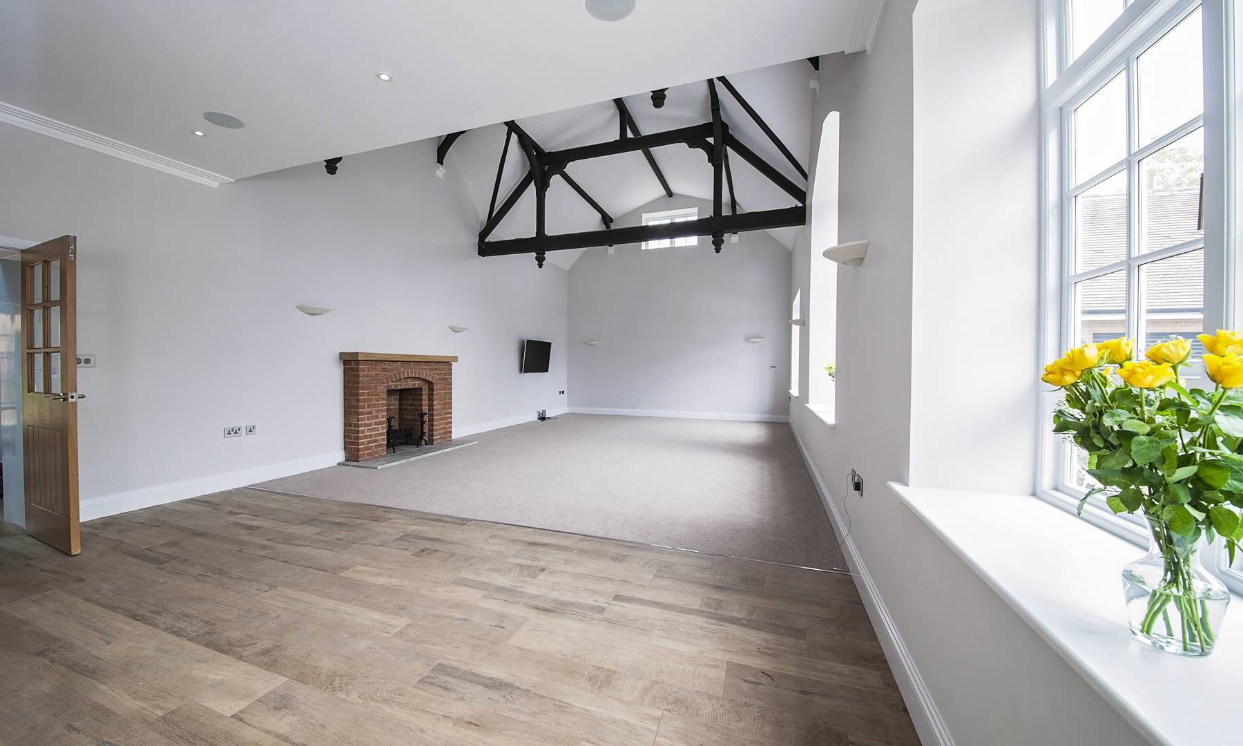 Spacious empty living room with a fire place and structural beams on the ceiling.