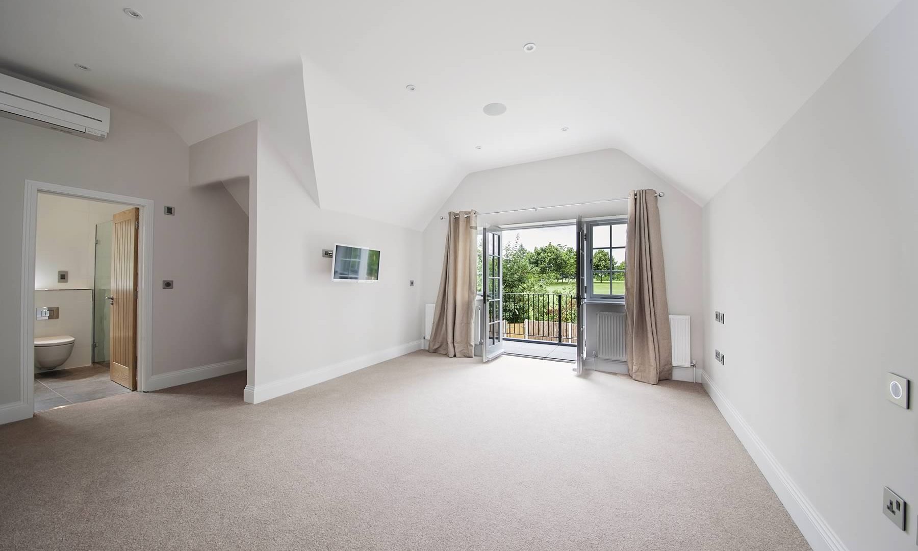 An empty bedroom with fitted carpet, ensuite and doors leading out to a balcony